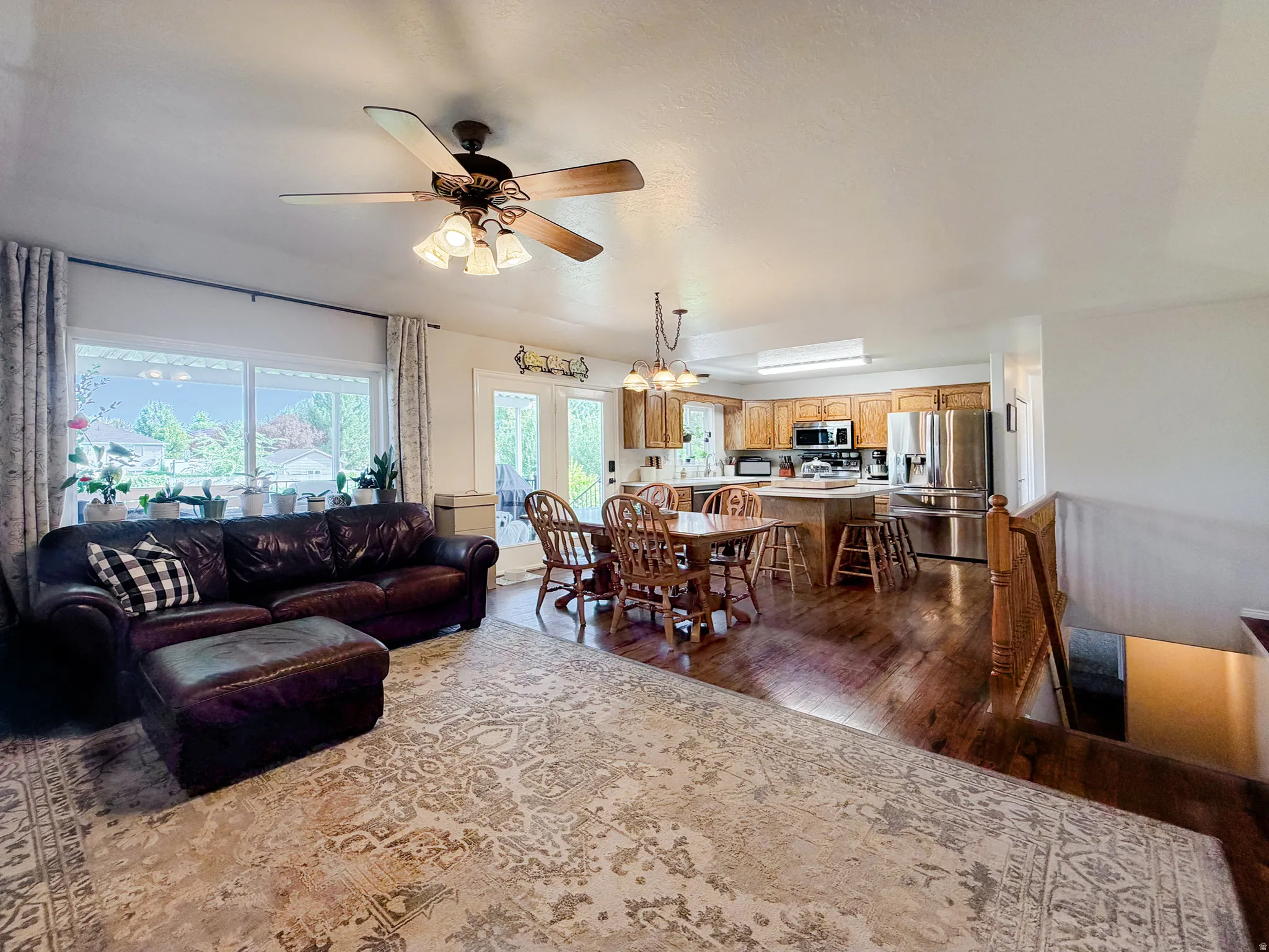 Open-concept living area with wood-finish flooring, a ceiling fan with integrated lighting, and a large window