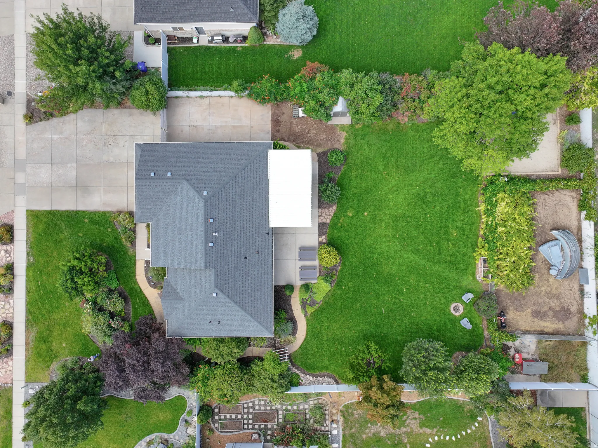 Expansive lot featuring a large lawn area, mature trees, concrete driveway, and varied landscaping