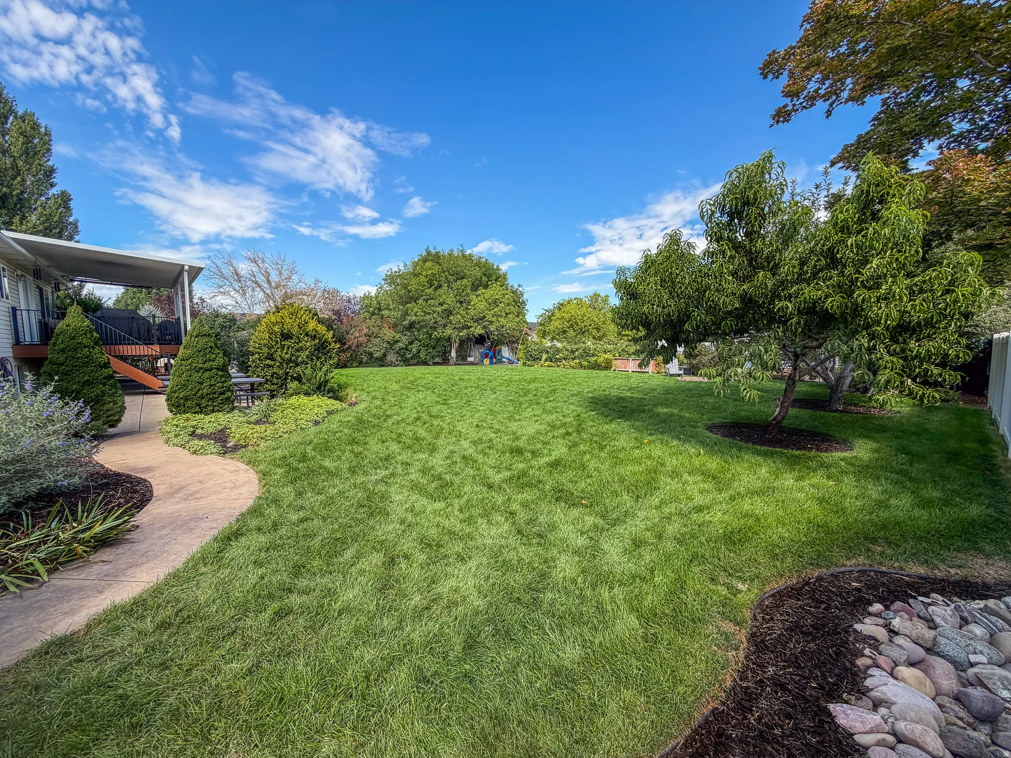 Expansive backyard featuring a manicured lawn, mature trees, and a decorative rock bed