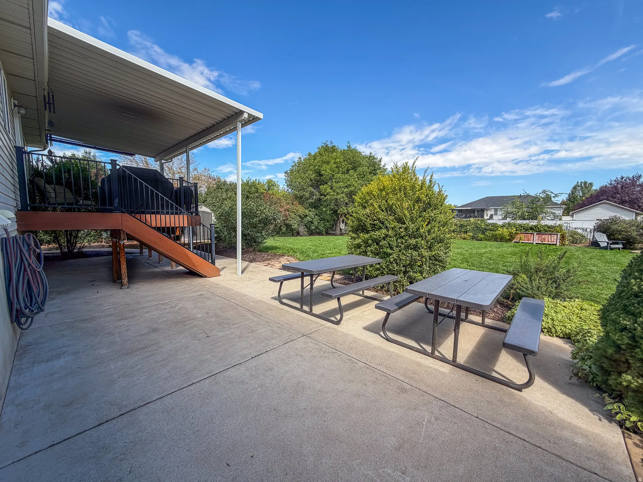 Expansive concrete patio with a covered section, featuring a raised deck with dark railing and a wood-finish staircase