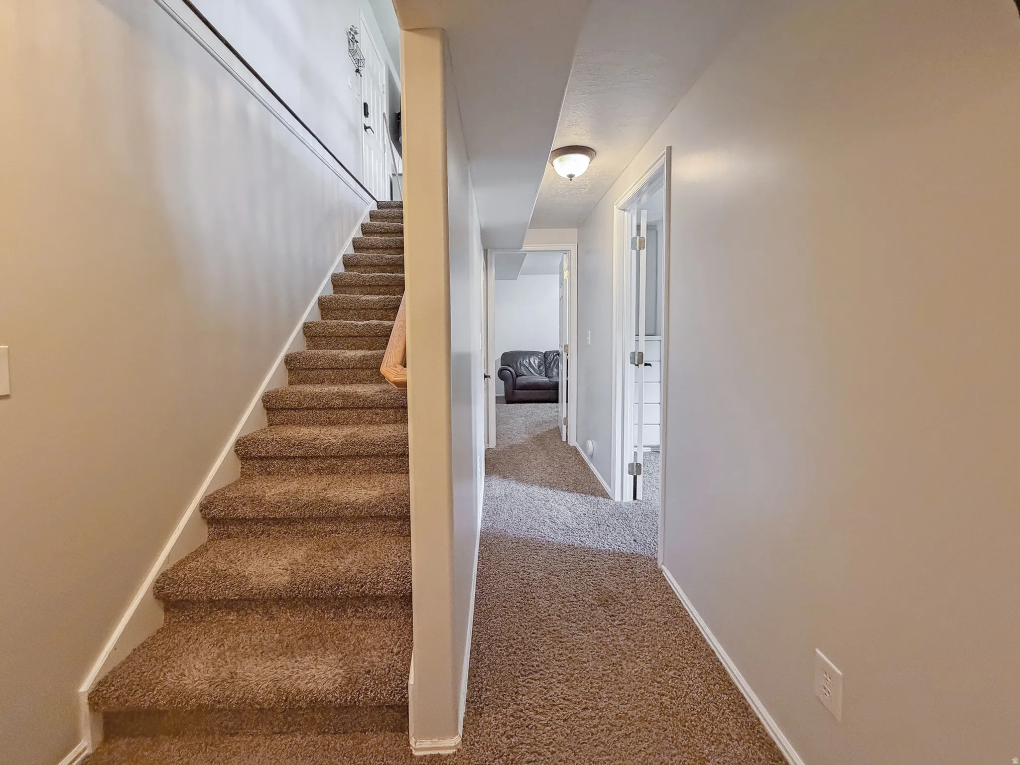 Carpeted staircase with white trim, leading to a hallway with recessed lighting