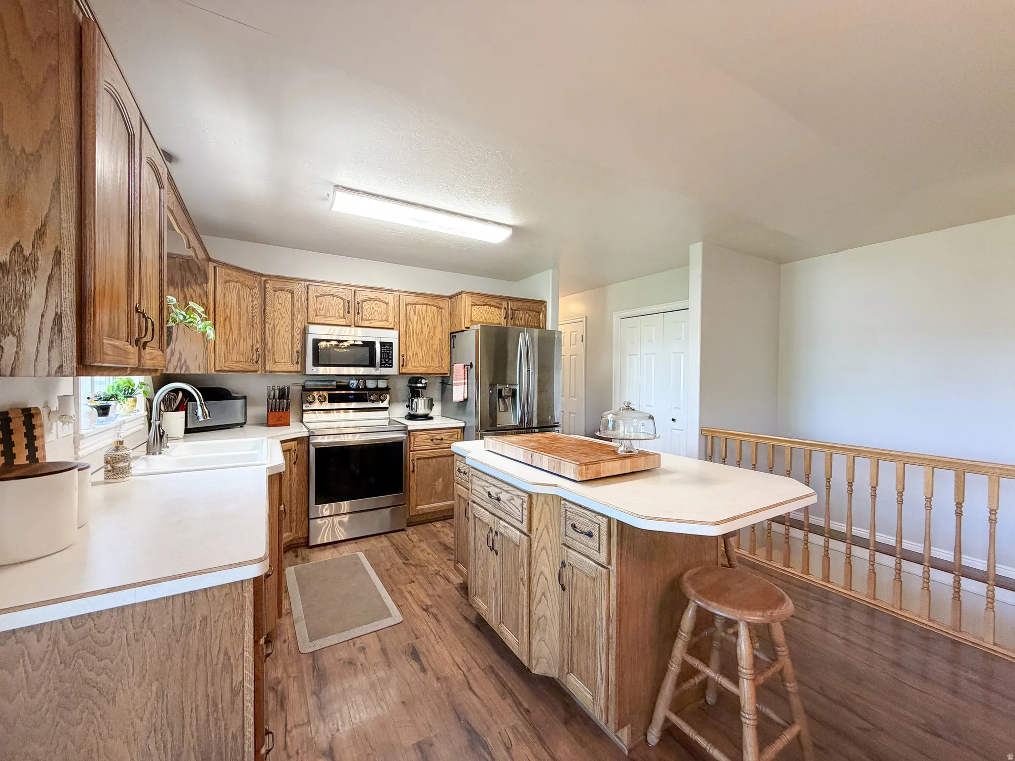 Kitchen featuring wood-finish flooring, wood cabinetry, stainless steel appliances, a center island with countertop seating, and a farmhouse-style sink