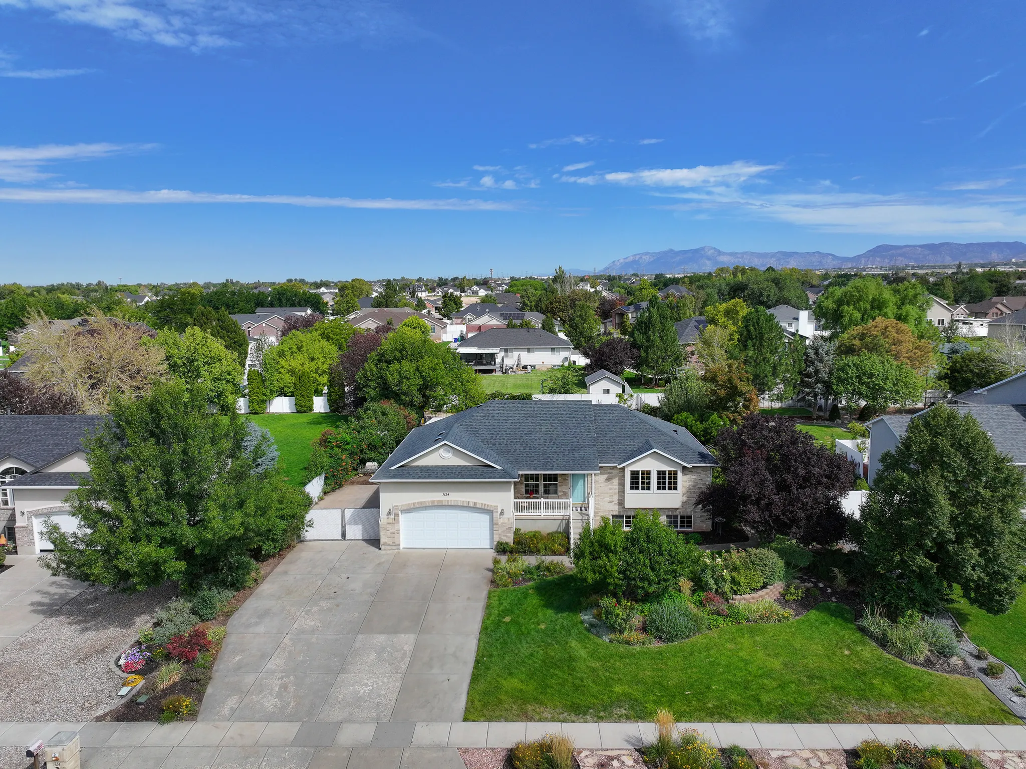 Paved driveway, attached garage, stone and siding exterior, landscaped front yard, and a shingle roof