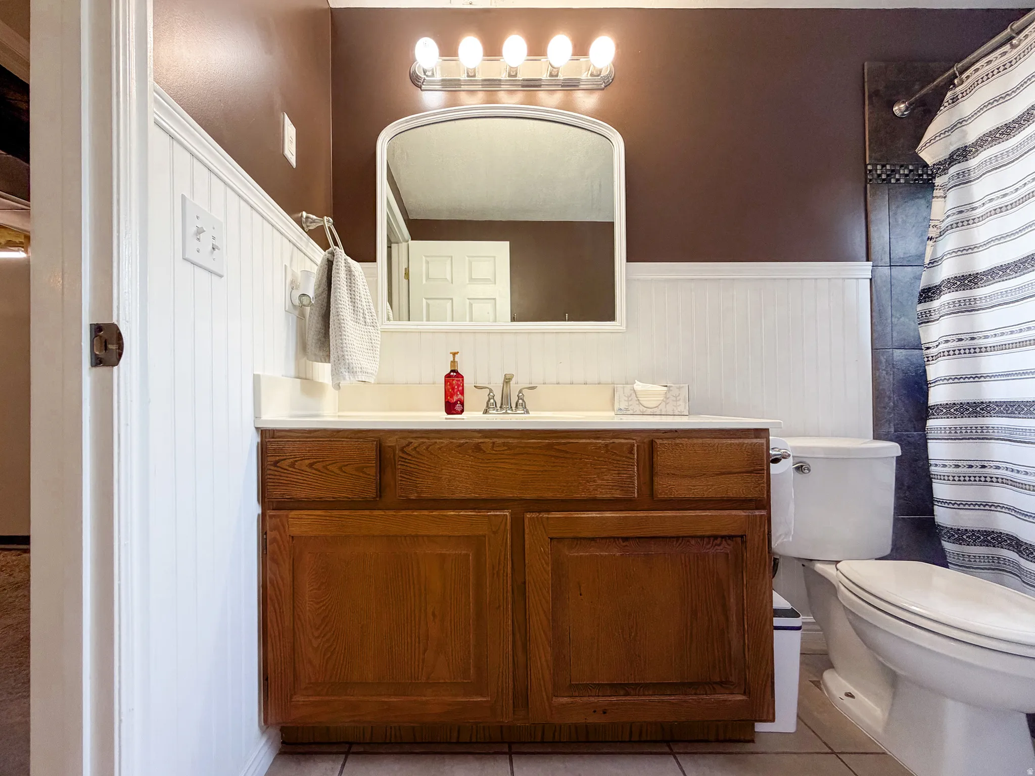 Wood-finish vanity with an integrated sink, polished chrome faucet, and overhead bar lighting