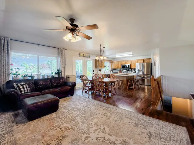 Open-concept living area with wood-finish flooring, a ceiling fan with integrated lighting, and a large window