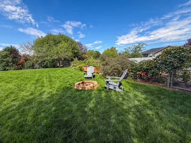 Expansive lawn with a stone-ringed fire pit, mature perimeter landscaping, and a chain-link fence