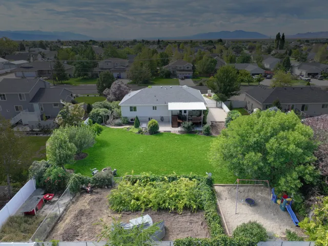 Expansive green lawn, mature perimeter trees, rear deck with partial covering, established garden area, and a dedicated play area