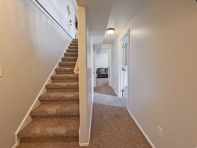 Carpeted staircase with white trim, leading to a hallway with recessed lighting