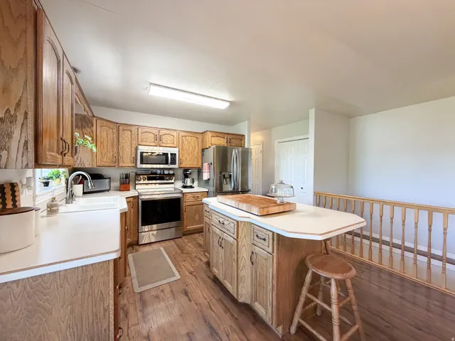 Kitchen featuring wood-finish flooring, wood cabinetry, stainless steel appliances, a center island with countertop seating, and a farmhouse-style sink