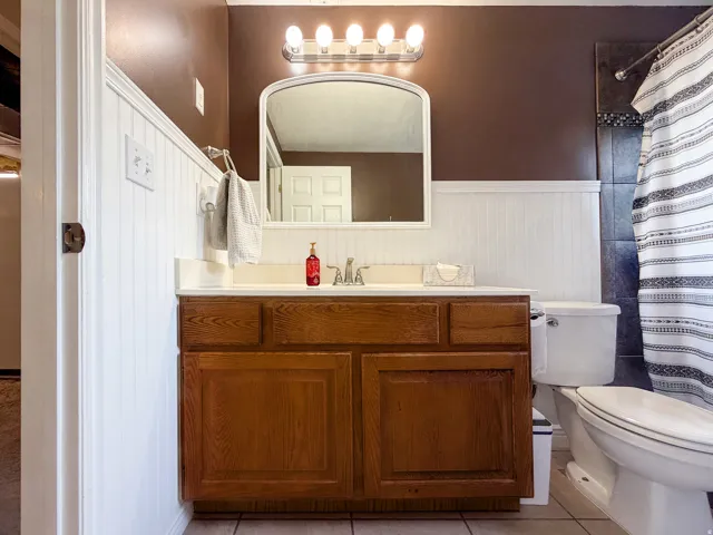 Wood-finish vanity with an integrated sink, polished chrome faucet, and overhead bar lighting