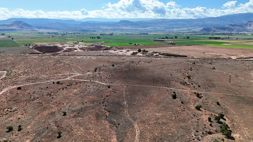 Expansive land featuring desert terrain, distant green fields, and mountainous scenery