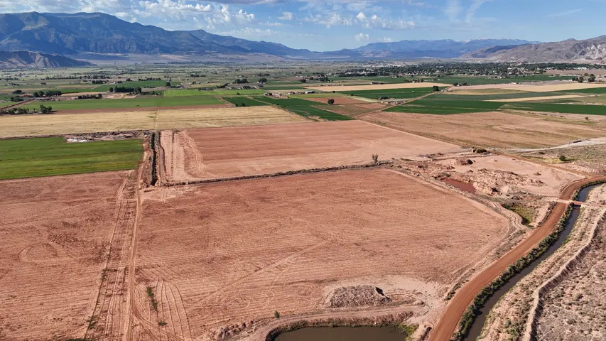 Expansive acreage featuring cultivated fields, a dirt road, and a water canal, all set against a backdrop of distant mountains