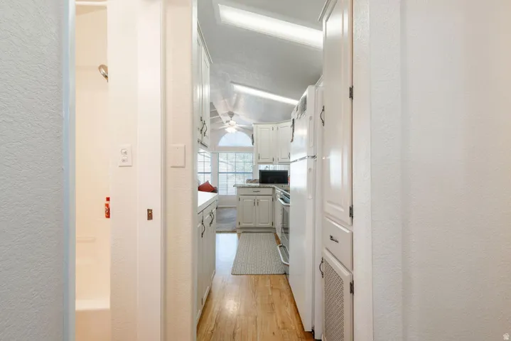 Kitchen featuring vaulted ceilings, wood-finish flooring, white cabinetry, and white appliances