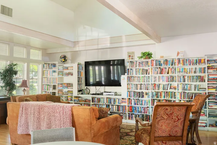 Vaulted ceiling with exposed beams, built-in shelving, large windows, wood-finish flooring