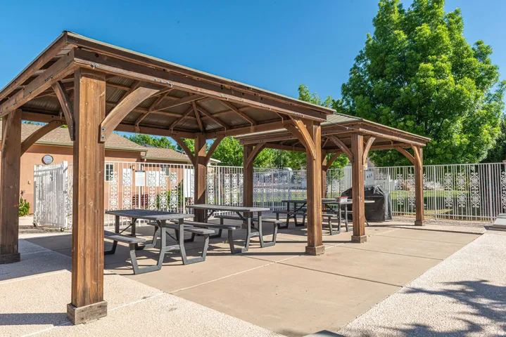 Outdoor patio featuring two wooden gazebos, concrete and gravel surfacing, and decorative metal fencing