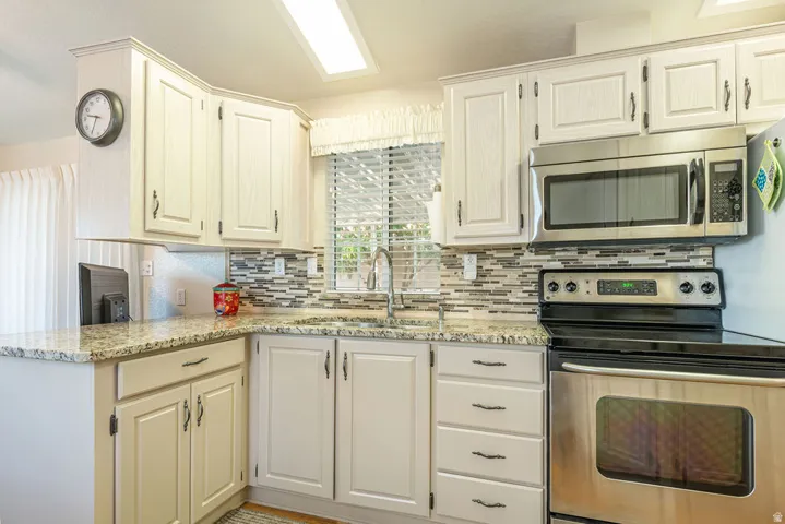 Kitchen featuring granite-style countertops, stainless steel appliances, white cabinetry with dark hardware, and a mosaic tile backsplash