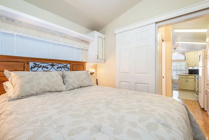 Bright bedroom featuring a wood-finish headboard with decorative tile inlay, layered bedding, dual nightstands with integrated lighting, horizontal blinds, and hardwood flooring