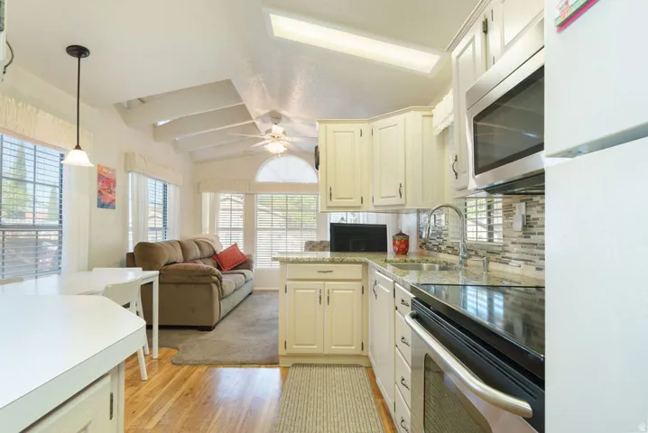 Vaulted ceiling with exposed beams, wood-finish flooring, kitchen with granite countertops, stainless steel appliances, and a tiled backsplash