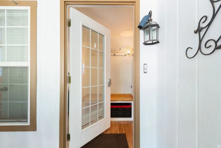 Glass-paneled entry door, wood-finish flooring, built-in bench, wall-mounted sconce, and window with blinds