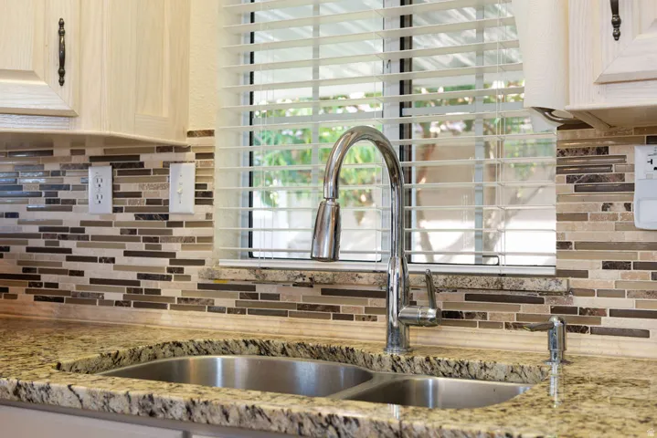 Double basin stainless steel sink with a high-arc faucet, granite-style countertop, and mosaic tile backsplash