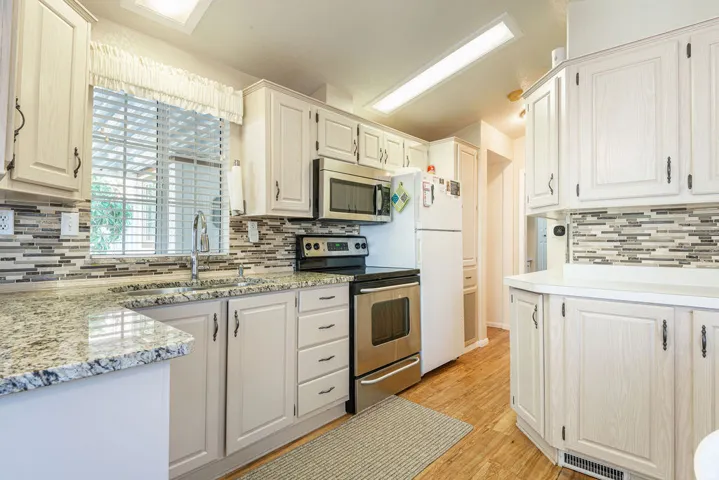 Kitchen featuring light-toned cabinetry, granite-finish countertops, stainless steel appliances, a mosaic tile backsplash, and wood-finish flooring