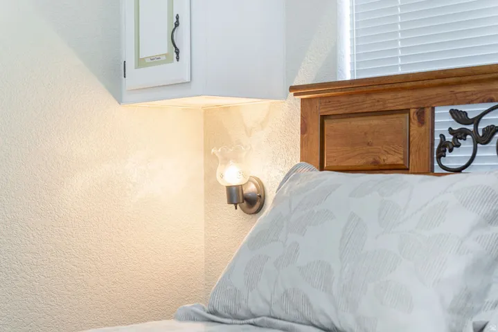 Built-in wall cabinetry with a decorative handle, wall sconce with a fluted glass shade, wood-finish headboard, and horizontal blinds