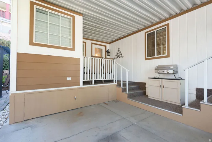 Covered concrete patio with built-in outdoor cabinetry, exterior steps with handrails, and vertical and horizontal panel siding