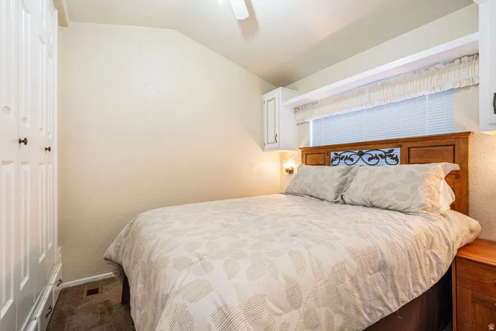 Carpeted room featuring a wood headboard with decorative metal inlay, sconce lighting, and built-in white cabinetry