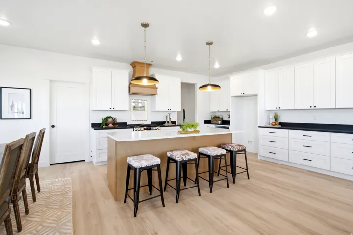 Light wood-finish flooring, white cabinetry, dark countertops, a central island with seating, and pendant lighting