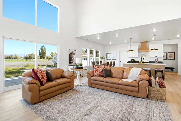 Bright, open-concept living area showcasing soaring ceilings with skylights, expansive glass doors opening to manicured grounds, and warm wood-finish flooring throughout