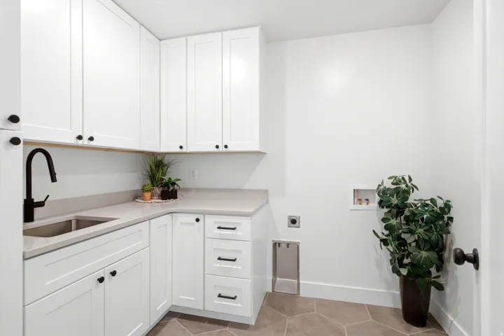 White shaker-style cabinetry with matte black hardware, light-toned countertop, stainless steel undermount sink with matte black faucet, and hexagonal floor tiling