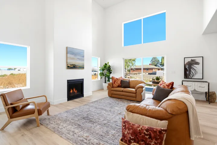 Vaulted ceilings, a built-in fireplace, multiple large windows, light wood-finish flooring, and crisp white walls create an airy living space
