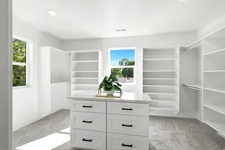 Expansive closet featuring integrated shelving, hanging rods, an island with drawer storage, and recessed lighting