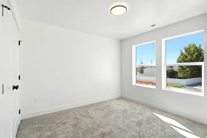 White painted walls, two large windows, gray carpet flooring, flush mount ceiling light, and white trim