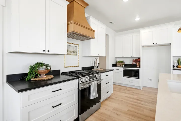 White shaker cabinetry with black hardware, black countertops, stainless steel range, built-in microwave, and wood-finish flooring