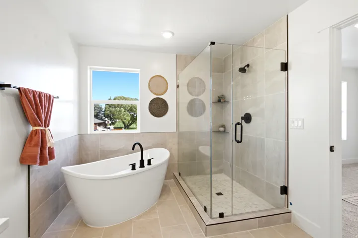 Freestanding soaking tub with matte black fixtures, glass-enclosed shower with tile surround, and light tile flooring