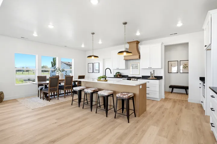 Open-concept kitchen and dining area featuring light wood-finish flooring, white cabinetry, a central island with a light-colored countertop, and a wood-finish range hood