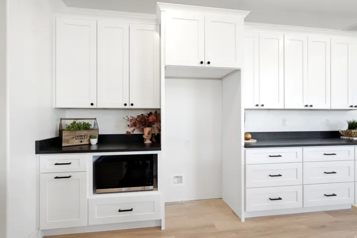 White shaker-style cabinetry with black hardware, dark countertops, built-in microwave, and wood-finish flooring
