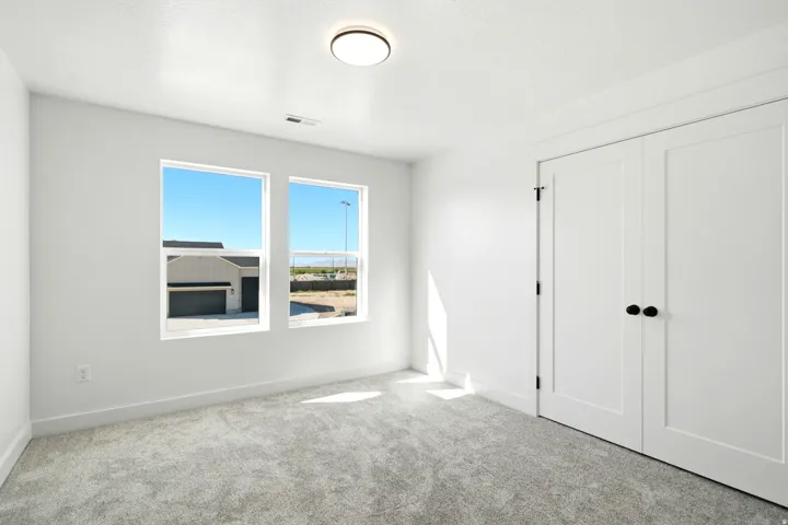 Plush carpet, white walls, flush mount ceiling light, dual windows, and bifold closet doors
