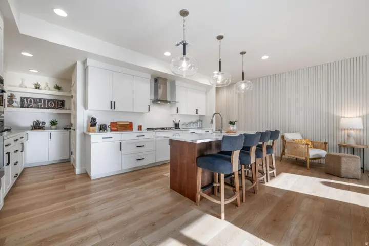 White cabinetry with matte black hardware, wood-finish flooring, a kitchen island with seating, pendant lighting, and a stainless steel range hood