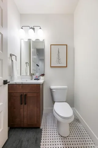 Hardwood-finish vanity with ample storage, white countertop, rectangular mirror, contemporary three-bulb vanity light, and basketweave tile flooring