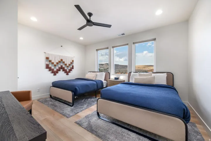 Bright dual-bedroom suite featuring multiple large windows framing expansive landscape vistas, wood-finish flooring, contemporary ceiling fan, and natural lighting throughout