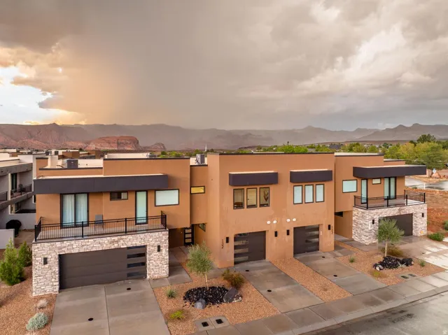 Contemporary exterior featuring a flat roofline, stucco finish, stone accents, and integrated garage doors