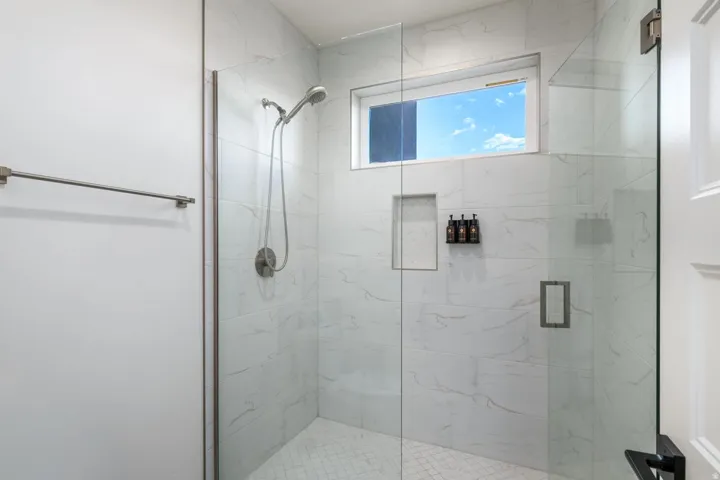 Glass-enclosed shower with white tiled walls, a built-in shower niche, and a window for natural light
