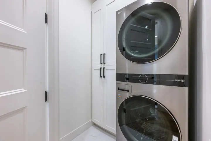 Stackable laundry appliances, white panel cabinetry with black hardware, and white baseboards