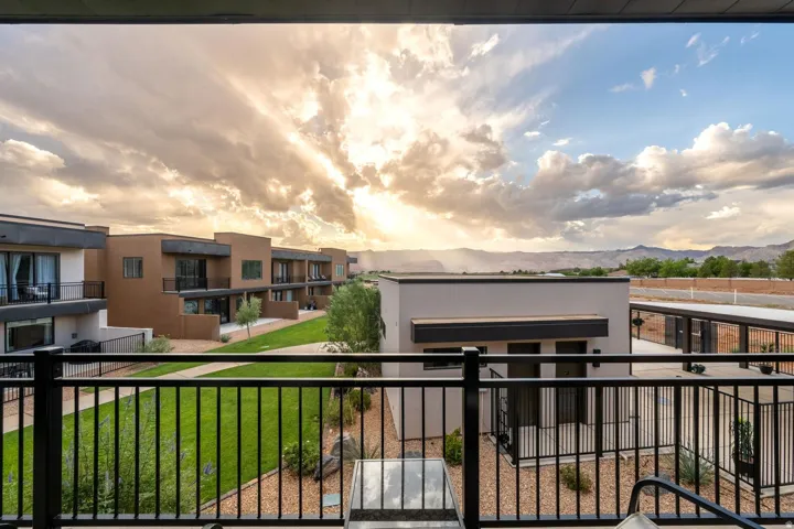 Black metal balcony railing overlooking a landscaped courtyard with green lawn and desert rock elements