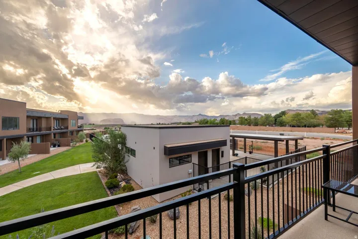 Black metal balcony railing, concrete flooring, exterior canopy, landscaped grounds with green lawn, and desert-style landscaping