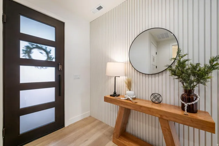 Dark-finished entry door with frosted glass panels, wood-finish flooring, and a decorative slatted wall