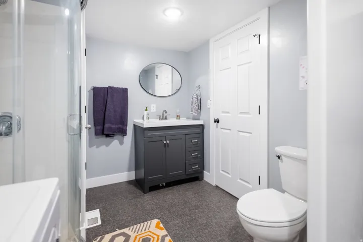 Modern bathroom featuring a glass-enclosed shower, a vanity with a white countertop, an oval mirror, and a white toilet