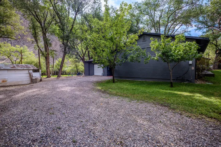 Gravel driveway with mature trees, green lawn, and a dark-toned exterior